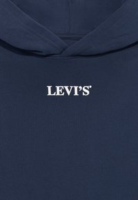 Tamsiai mėlyna gobtuvė pagaminta iš minkštos medžiagos, su balta "LEVI'S" logotipu ant krūtinės, atsipalaidavusio silueto ir gobtuvu.