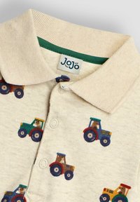 Polo enfant en coton beige, avec un motif de tracteurs colorés. Col côtelé et patte de boutonnage avec bord vert sous le col.