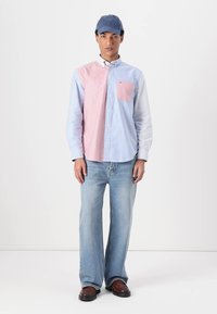 Camicia a maniche lunghe con un design a blocchi di colore blu chiaro e rosa, dotata di taschino, abbinata a un paio di jeans azzurri larghi e scarpe marroni.
