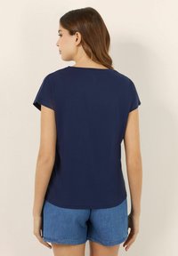 Mörkblå kortärmad skjorta med rund halsringning, matchad med ljusa denimshorts, som visar en mjuk textur och avslappnad passform.