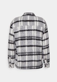 Camisa casaco xadrez cinza e branca com uma textura macia semelhante à lã, apresentando um colarinho clássico e punhos com botões. A vista traseira mostra um detalhe de pala.