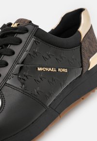 Czarne sneakersy z teksturowanym, lakierowanym wykończeniem oraz wytłoczonym logo "MK". Złote akcenty po bokach, gumowa podeszwa i czarne sznurowadła.