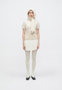 Krémový top zo zmesi vlny s krátkymi rukávmi a zodpovedajúcim šálom, v kombinácii so skladanou, svetlou sukňou a telovými pančuchami, čierne balerínky.