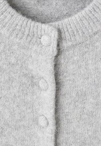Cardigan de punto gris claro con cuello acanalado y tres botones texturizados en la parte delantera. Material suave y difuso similar a la lana, con sutiles variaciones.