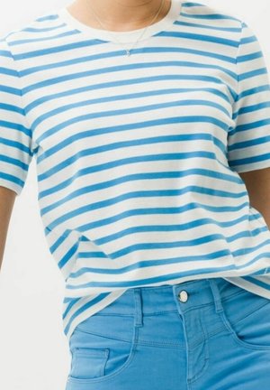 T-shirt rayée en blanc et bleu clair, fabriquée en coton doux. Encolure ronde et manches courtes. Associée à un jean bleu clair avec un bouton à l'avant.