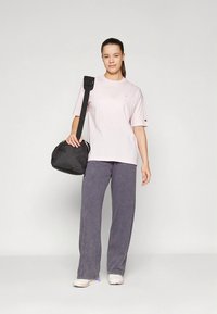 Camiseta de algodón rosa con mangas cortas, combinada con pantalones anchos grises y un bolso de hombro negro. Incluye un detalle de logo en la camiseta.