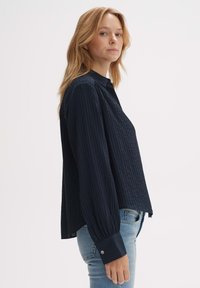 Navy blue long-sleeve shirt with a ribbed texture, buttoned cuff, and a relaxed fit. Worn with light blue jeans, showcasing a side view.
