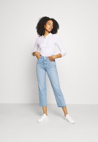 Ljuslila långärmad polo med knappstängning, matchad med ljusblå högmidjade raka jeans och vita sneakers.