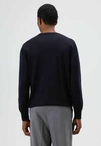 Marineblauwe gebreide trui met lange mouwen en een ronde hals, gecombineerd met grijze tailored pantalon. Soepele textuur en minimalistisch ontwerp.