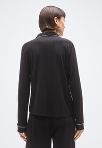 Mustast pikkade varrukatega topp kraega, mille varrukatel ja allääre juures on valged äärised. Sile ja pehme kangas ning lõdvestunud istuvus.