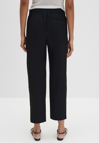 Zwarte, wijde broek met een elastische tailleband, voorzien van een achterzak en rechte pijpen, gemaakt van een glad materiaal.