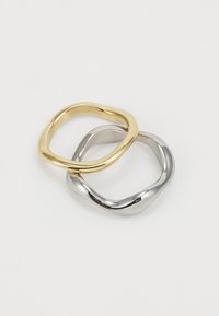 Dos anillos entrelazados, uno de oro y otro de plata. Ambos tienen una forma suave y redondeada, con un acabado brillante y un diseño de sutil torsión.