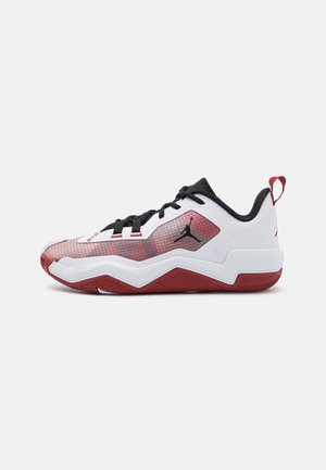Niski sportowy sneaker w białym i czerwonym kolorze z czarnymi sznurowadłami, teksturowaną podeszwą i logo Jumpman po boku oraz na języku pięty.