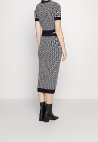 Sukienka dzianinowa z geometrycznym czarno-białym wzorem, dopasowanym krojem, krótkimi rękawami i długością do kolan, zestawiona z czarnymi botkami za kostkę.