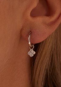 Silver hoop earring featuring a floral charm, adorned with clear gemstones, hanging from the hoop near the earlobe.