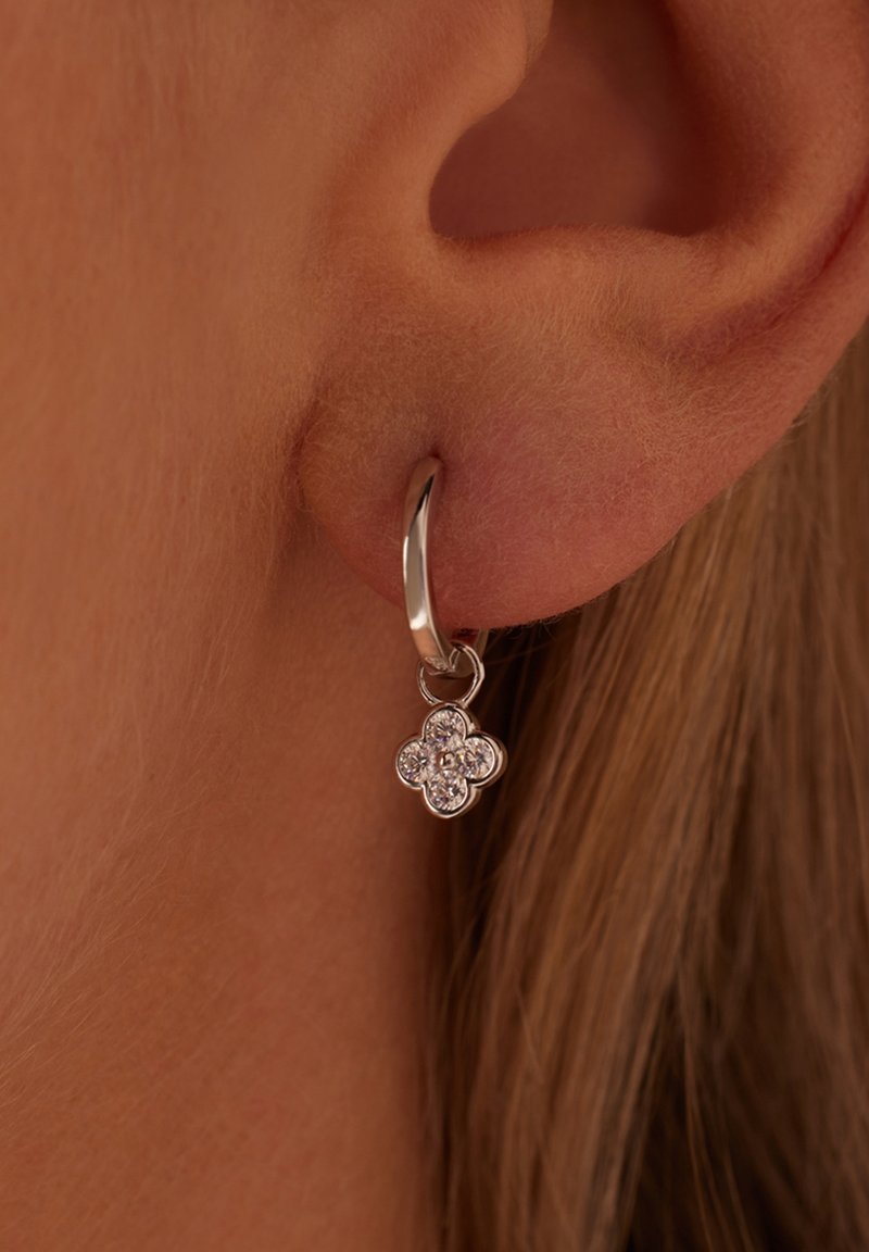 Silver hoop earring featuring a floral charm, adorned with clear gemstones, hanging from the hoop near the earlobe.