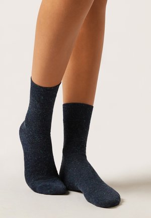 Calcetines azul marino hechos de tela texturizada, con motas verdes, de altura al tobillo, con puños acanalados y suelas lisas.