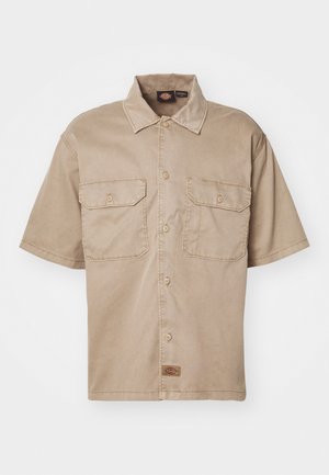 Trumpas rankovės, smėlio spalvos marškiniai, pagaminti iš medvilnės, su mygtukų užsegimu, dviem krūtinės kišenėmis ir maža prekės ženklo etikete apačioje.