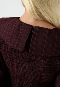 Abito bordeaux con colletto a quadretti, caratterizzato da un corpetto arricciato e una zip sul retro. Il tessuto ha un aspetto testurizzato e arricciato.