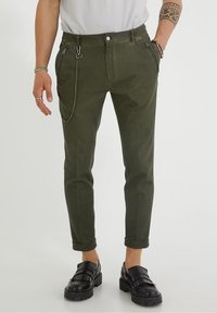 Olive zelené kalhoty se zužujícími se nohavicemi, poutky na pásek, předními kapsami a stříbrným řetízkovým detailem. Vyrobené z texturované látky, mají ohrnutý lem.