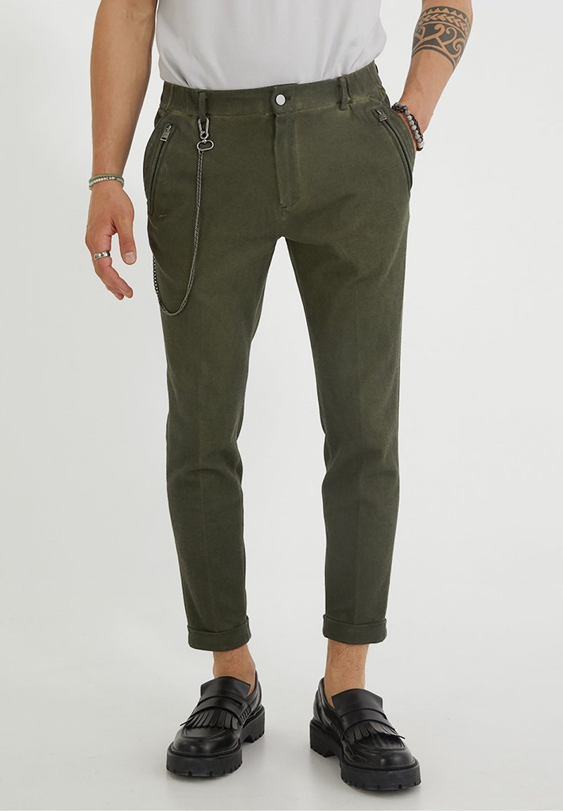 Olive zelené kalhoty se zužujícími se nohavicemi, poutky na pásek, předními kapsami a stříbrným řetízkovým detailem. Vyrobené z texturované látky, mají ohrnutý lem.
