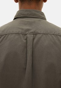 Widok z tyłu osoby ubraną w ciemnooliwkową koszulę z kołnierzykiem i zakładką na środku pleców.