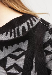 Pull noir et gris à motif avec un design abstrait, comportant un accent en anneau argenté sur la bretelle et une finition en tricot texturé.
