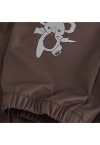 Brunt tyg med en ljusgrå koalain grafik. Materialet har en jämn textur med elastiska rynkor i kanterna.