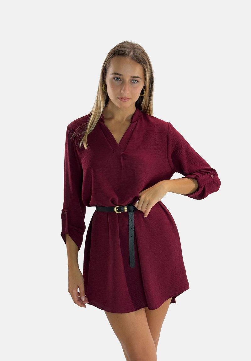 Robe bourgogne à col en V et manches longues, avec des poignets roulés et une ceinture noire à la taille, réalisée en tissu lisse et texturé.