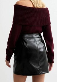 Suéter de punto burdeos con escote asimétrico, combinado con una falda mini de cuero negro de cintura alta con un acabado brillante.