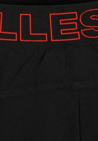Cinturilla de tela negra con letras rojas contorneadas "LLES" cosidas en la banda elástica de una prenda.