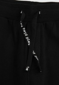 Czarne dresy z prążkowanym paskiem w talii, sznurkiem z napisem "red play" oraz miękkim, teksturowanym materiałem.