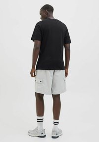 Sort bomulds t-shirt og lysegrå cargo shorts med to sidelommer, parret med hvide socks med sorte striber og grå sneakers.