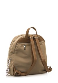 Mochila de tela color canela con detalles de cuero marrón, correas ajustables, compartimentos con cremallera y un detalle decorativo de cuerda en el lateral.