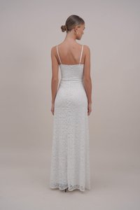 Rochie lungă din dantelă albă, cu bretele subțiri, bust ajustat și fustă fluidă. Prezintă un model floral și un material neted, texturat.