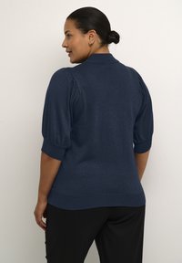 Top a maniche corte in maglia blu navy con una leggera lucentezza, dotato di colletto e maniche a sbuffo, abbinato a pantaloni neri.