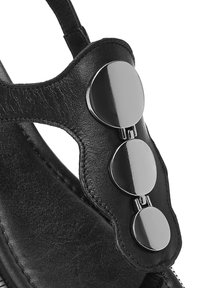 Sandalo in pelle nera con un design a intaglio curvo e tre accenti metallici lucidi sulla parte superiore. Dettagli della superficie testurizzata visibili.