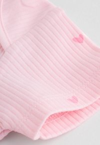 Tessuto rosa a coste con una texture morbida, caratterizzato da piccoli motivi a cuore, dettaglio di cucitura sul bordo e una forma arrotondata all'apertura.