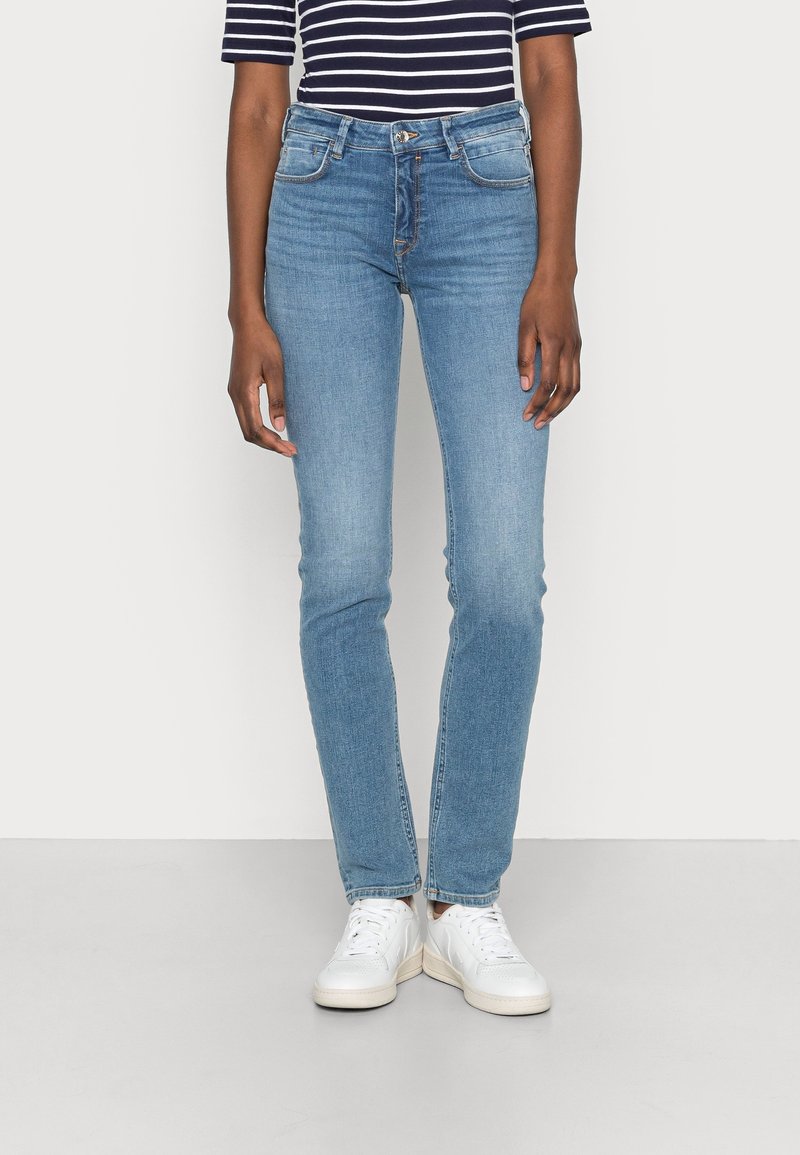 Light blue denim jeans with a slim fit, high waist, and subtle fading; worn with a navy and white striped short-sleeve top and white sneakers.