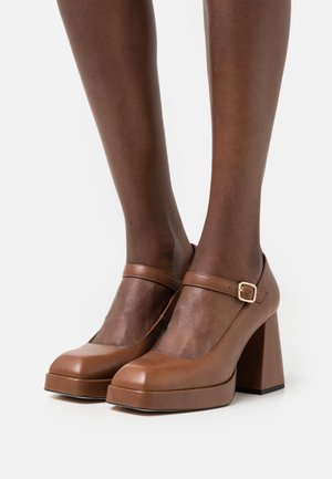 Hnědé kožené lodičky Mary Jane se čtvercovou špičkou, robustním blokovým podpatkem a páskem kolem kotníku se zlatou kovovou přezkou.