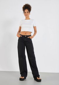 Μαύρο παντελόνι με φαρδύ πόδι και λεία υφή, με μπροστινές τσέπες, σε συνδυασμό με λευκό εφαρμοστό κοντομάνικο τοπ. Το σύνολο ολοκληρώνουν πλατφόρμα σανδάλια με επίπεδη σόλα.