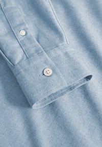 Light blue cotton shirt featuring a buttoned cuff, smooth texture, and subtle stitching details along the seam and button placket.