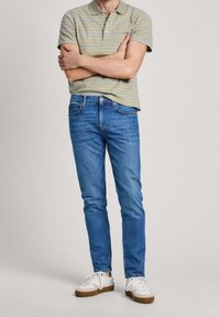 Herrkortärmad pikétröja i olivgrönt med vita och ljusblå ränder, kombinerad med blå jeans i denim och vita sneakers.