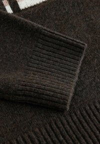Brązowy sweter wełniany z prążkowanymi mankietami i subtelnymi detalami tekstury. Tkanina wydaje się miękka i ciepła, z różnorodnymi wzorami dzianiny.
