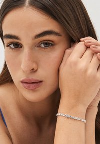 Silberarmband mit klaren, runden Kristallen, das ein filigranes Design am Handgelenk betont. Glatte Hautstruktur bei sanfter Beleuchtung.