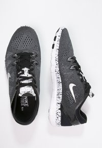 Sorte og grå atletik sko med mesh overdel, hvide teksturerede såler og et fremtrædende Nike-logo. Har snørebånd og en mønstret sål.