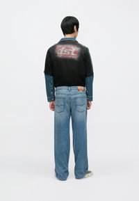 Fekete és kék farmerdzseki vörös logóval a háton, világoskék, bőszárú farmerral kombinálva, hátoldali zsebekkel és laza szabással.