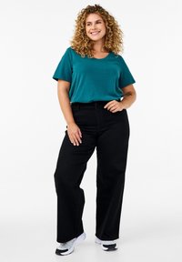 Teal kortærmet t-shirt med rund halslinje, parret med højtaljede sorte brede bukser; båret med grå og sorte sneakers.