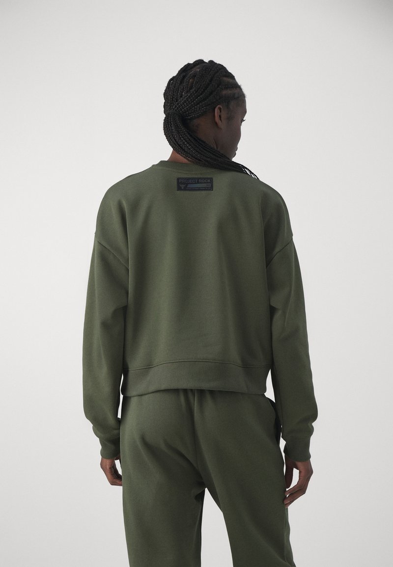 Grünes Baumwoll-Sweatshirt mit gerippten Bündchen und Saum. Mit einem Etikett mit "PROJECT ROCK"-Branding auf der Rückseite. Kombiniert mit passenden Hosen.