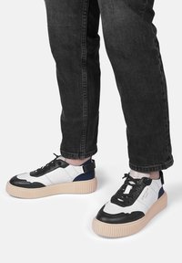 Baskets noires et blanches avec une semelle épaisse beige, un tissu texturé, des lacets noirs et un accent bleu sur le talon. Portées avec un jean sombre.